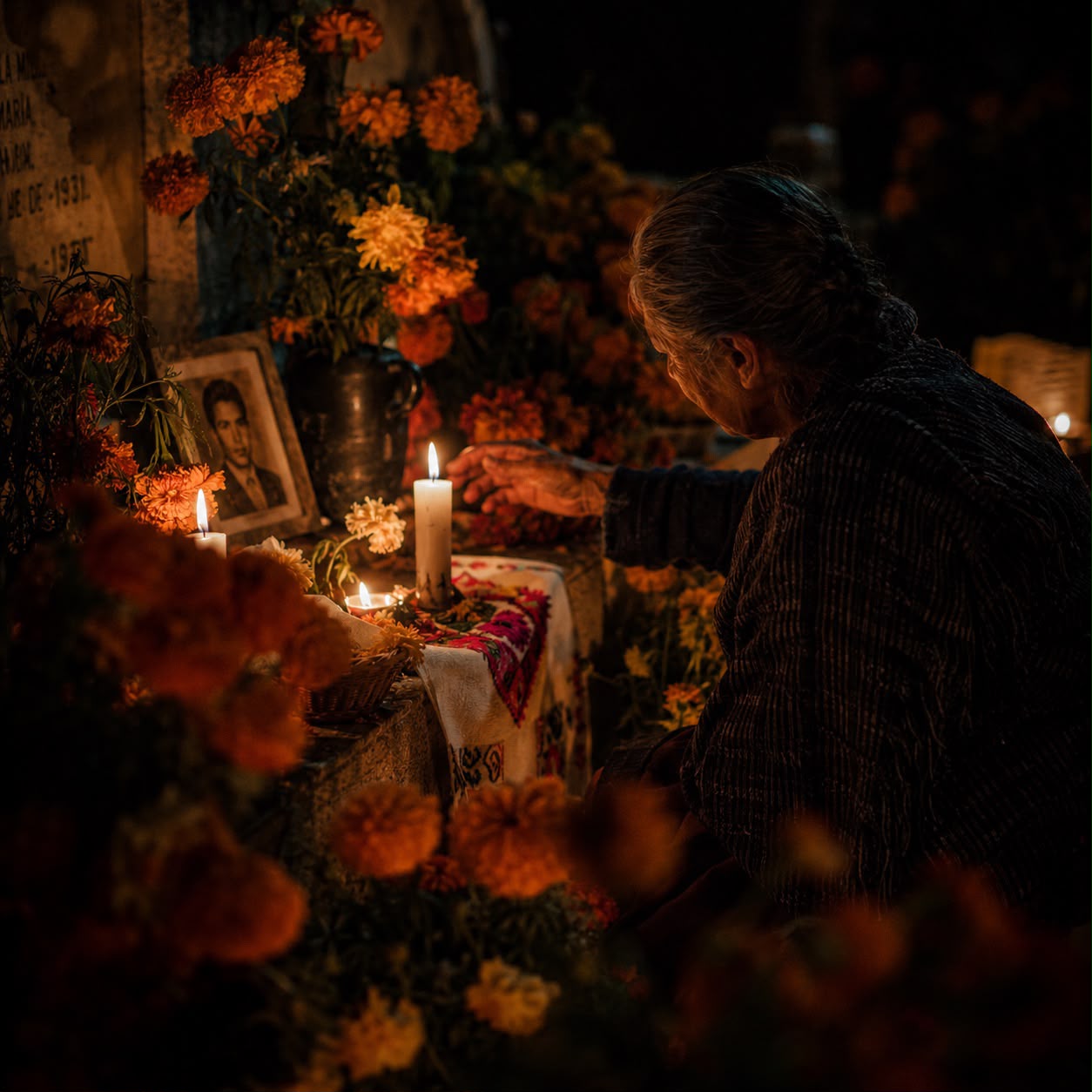 Una mujer vela una tumba en Noche de Muertos, con el retrato de un joven entre cempasúchil